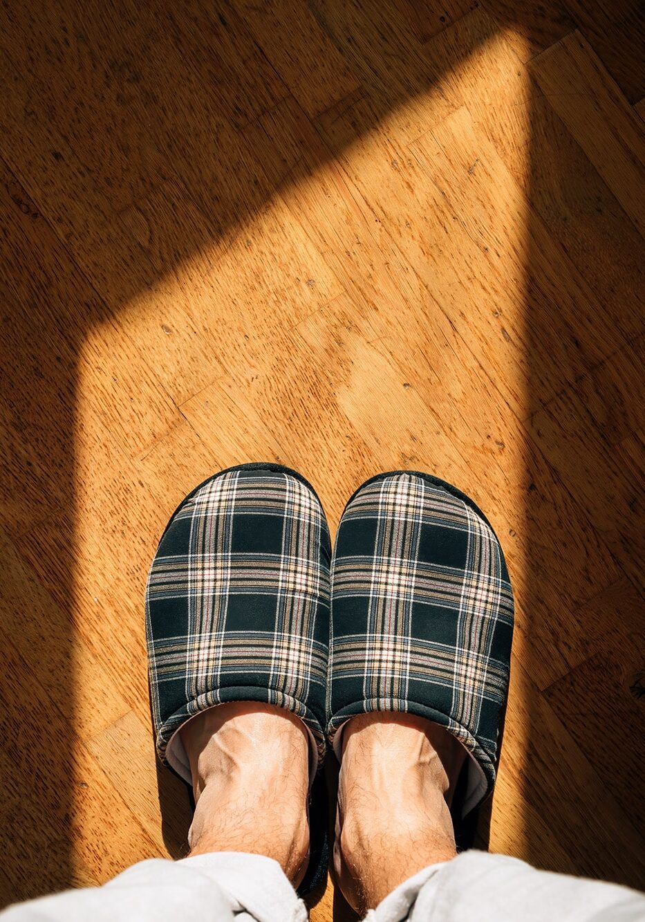 Top view of male feet wearing home slippers and standing on hardwood flooring in living room, copy space included